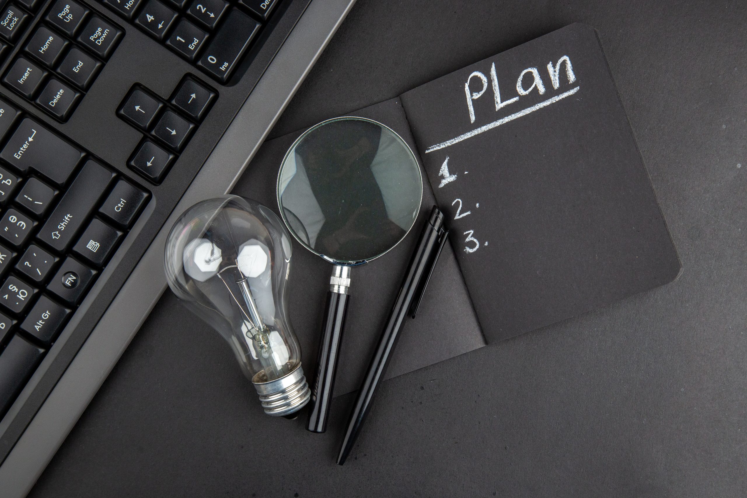 top view plan written black notepad lupa keyboard light bulb pen black table